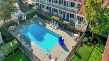 A two-story building with a swimming pool, lounge chairs, and a fenced patio area.