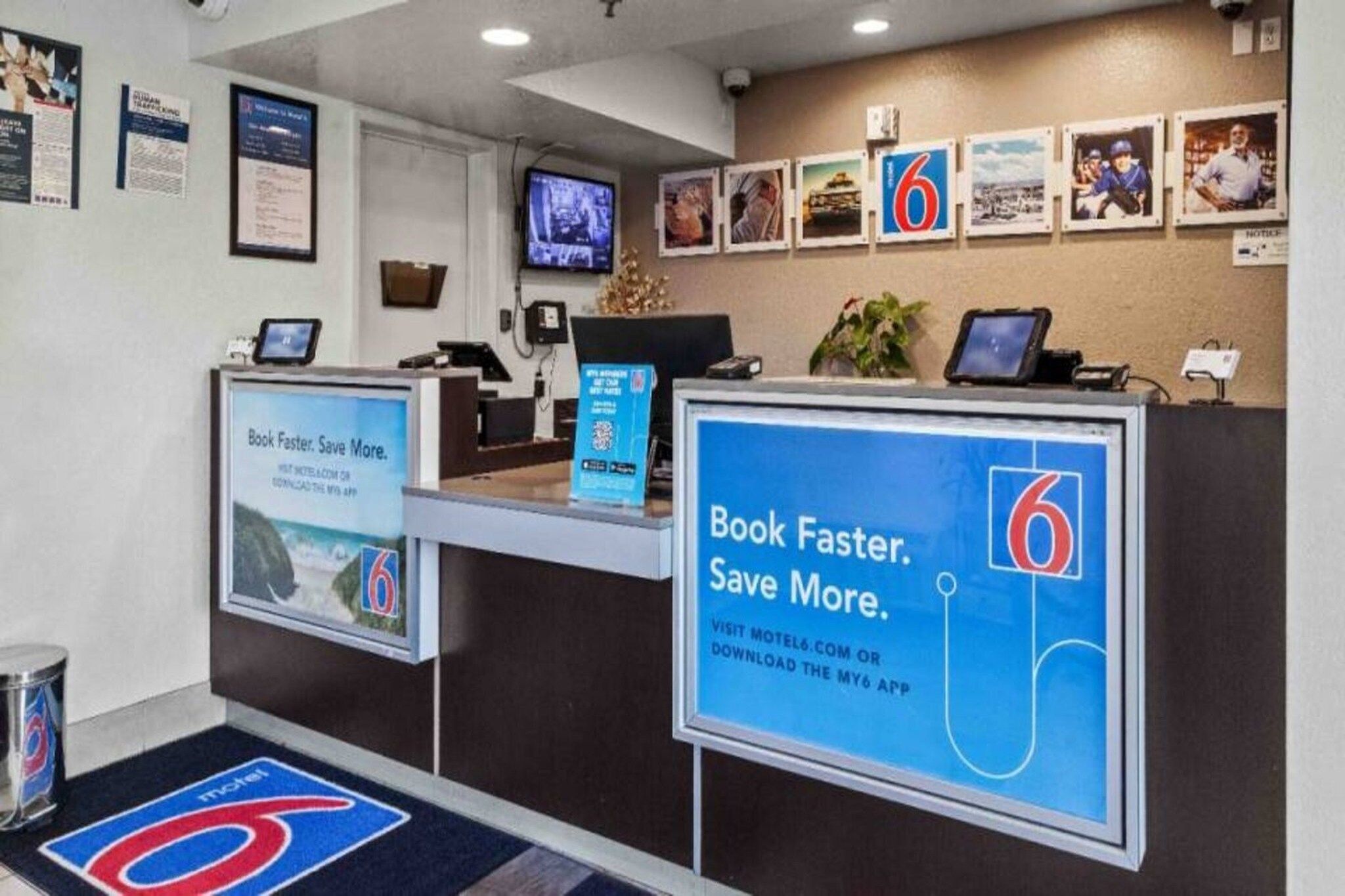 A motel reception desk with a large sign advertising the motel's app, a television, and framed pictures on the wall.
