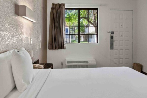 Een hotelkamer met een bed, nachtkastje, telefoon, raam met gordijnen en een deur.