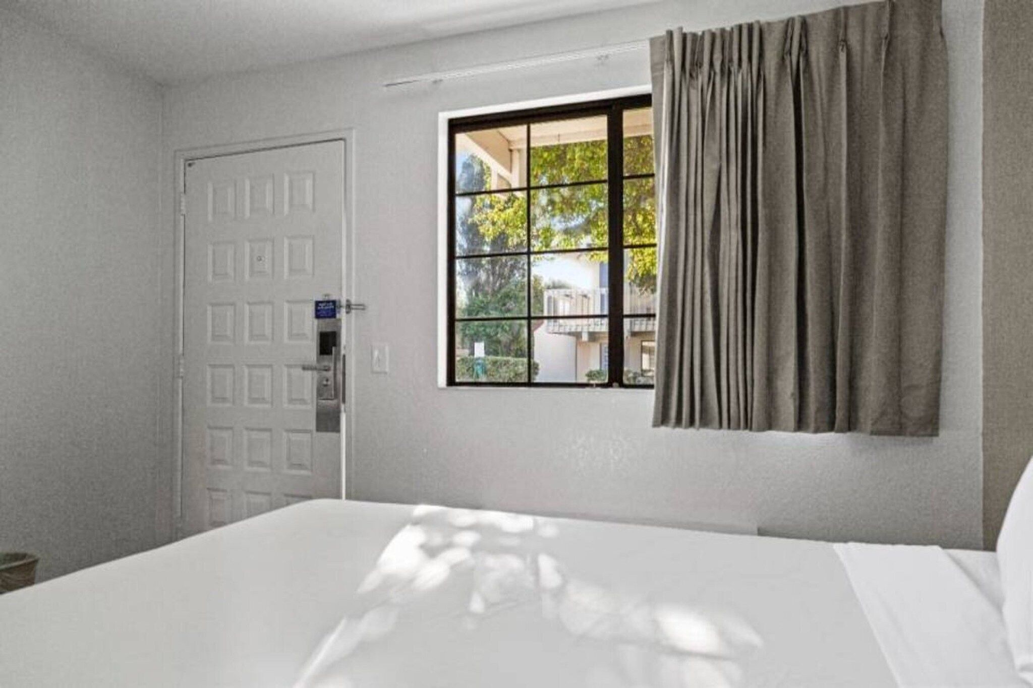 Ein Hotelzimmer mit einem Bett, einem Fenster mit Vorhängen und einer Tür.