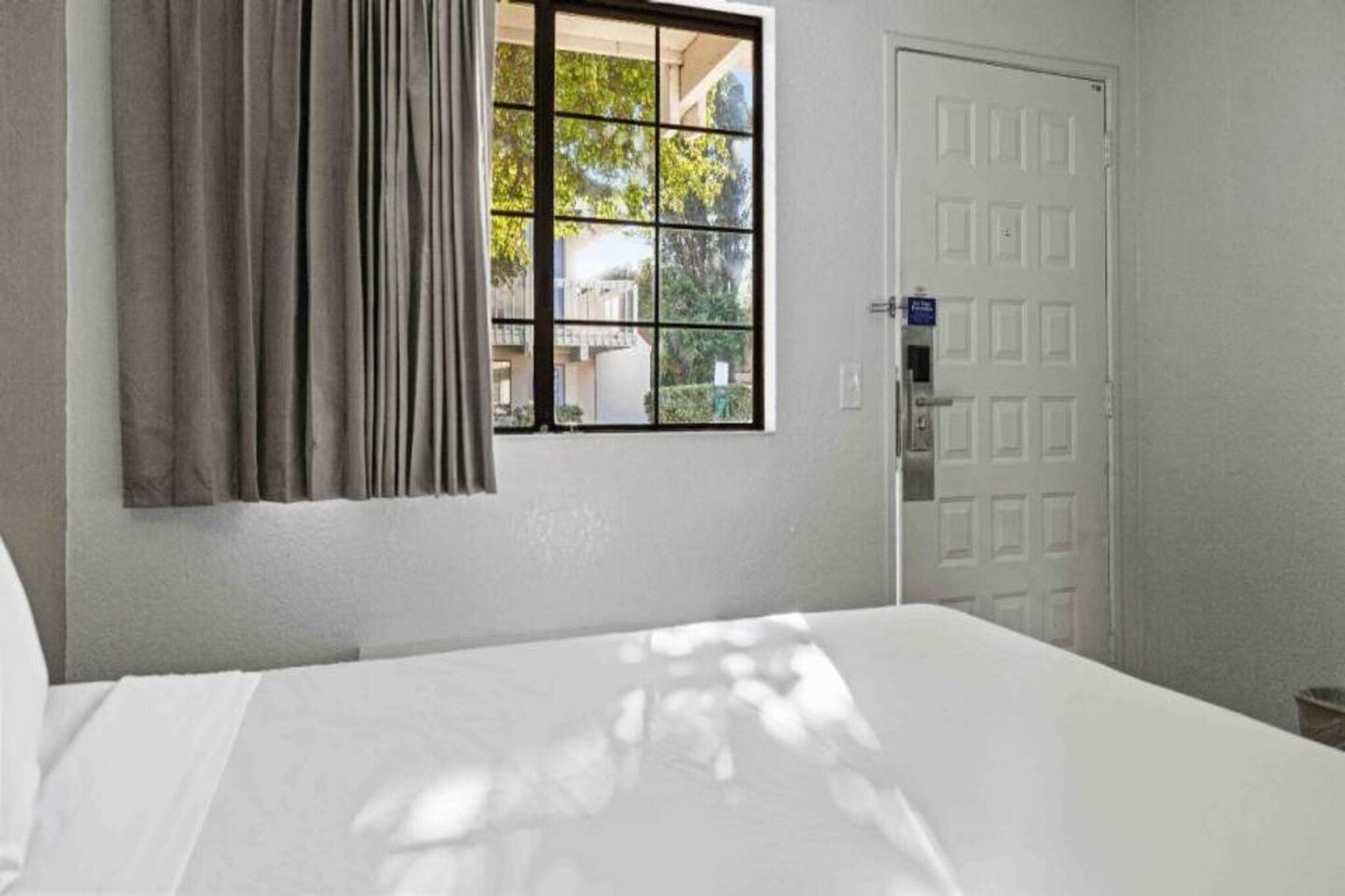 A hotel room with a bed, a window with curtains, and a door.