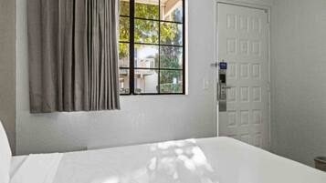 A hotel room with a bed, a window with curtains, and a door.