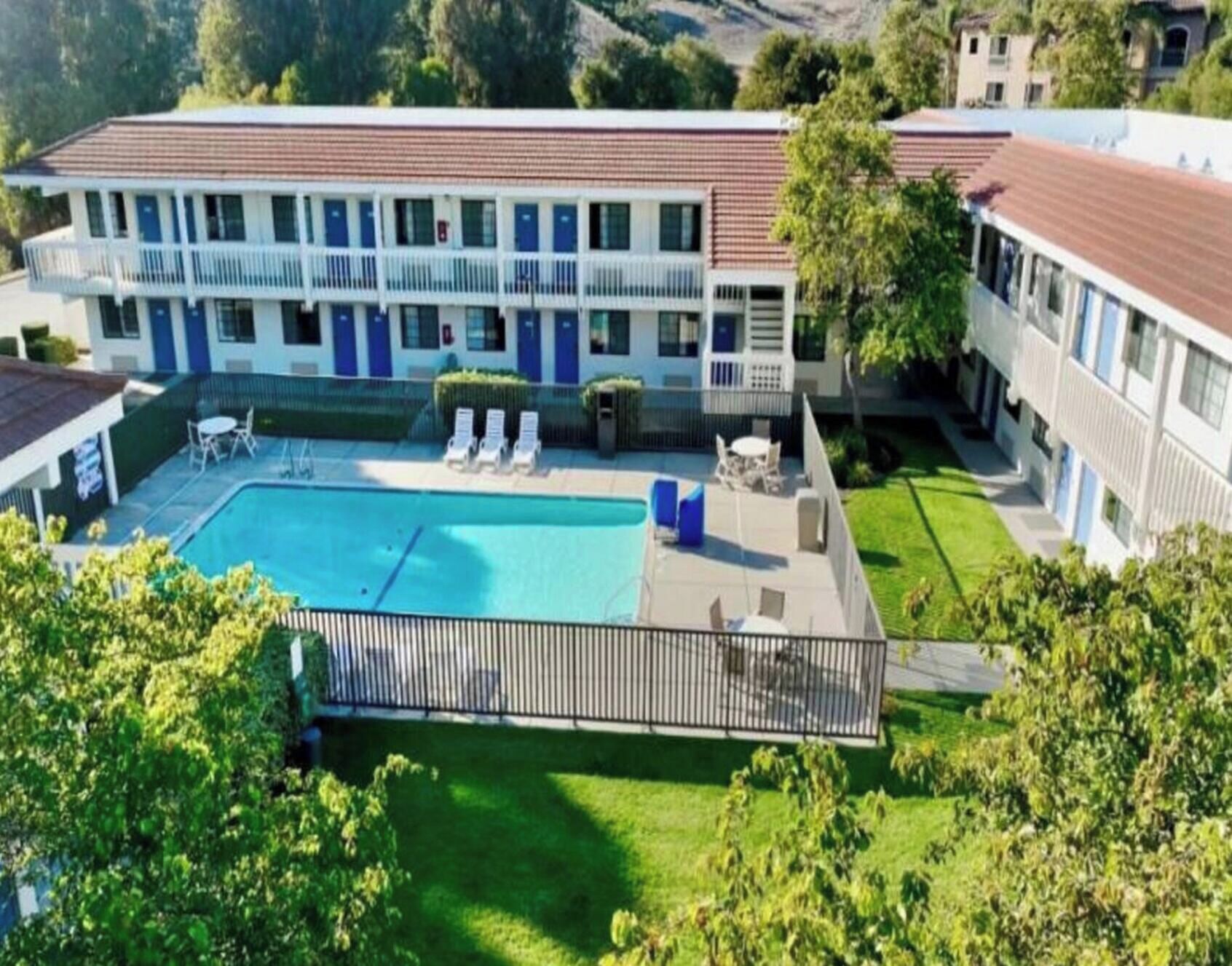 A hotel with a swimming pool, lounge chairs, and a fenced patio area.