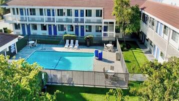 A hotel with a swimming pool, lounge chairs, and a fenced patio area.