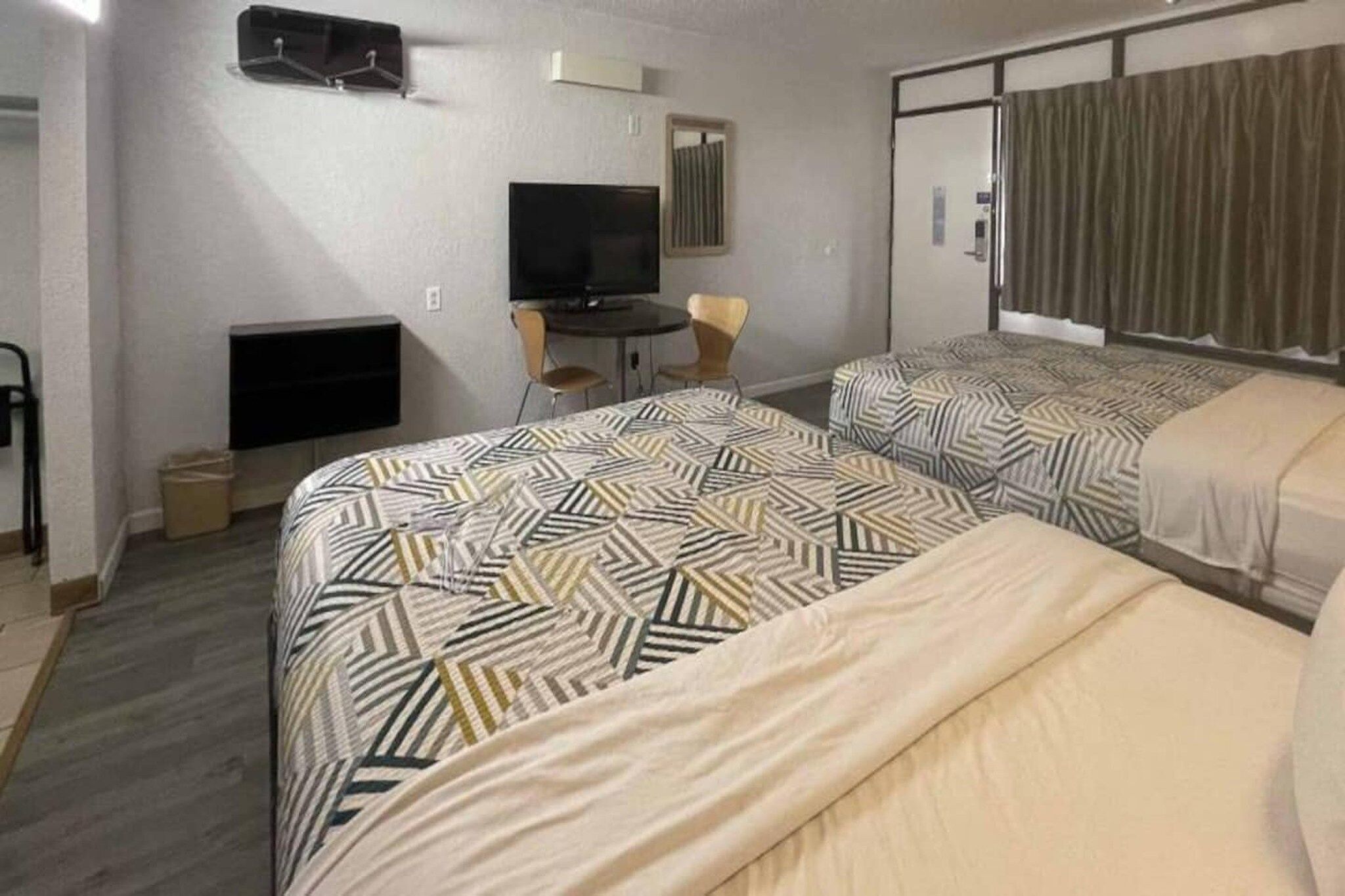 Ein Hotelzimmer mit zwei Betten, einem Schreibtisch, einem Fernseher und einem Fenster mit Vorhängen.