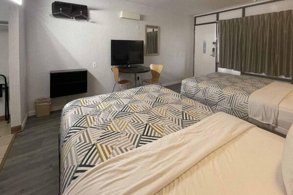Habitación de hotel con dos camas, un escritorio, un televisor y una ventana con cortinas.