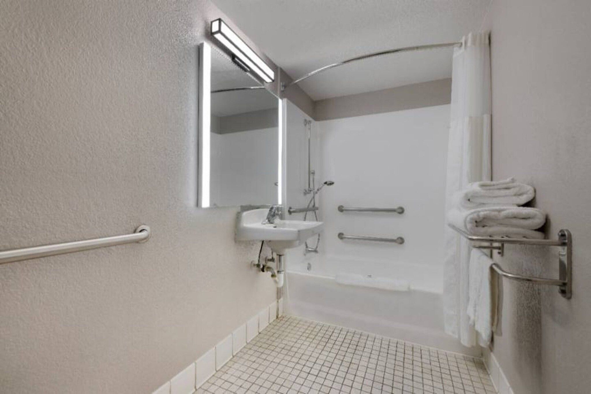 A bathroom with a white sink, a mirror, a shower, and a towel rack.
