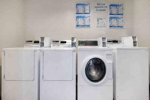 A row of white front-loading washing machines in a laundry room with informational posters on the wall.