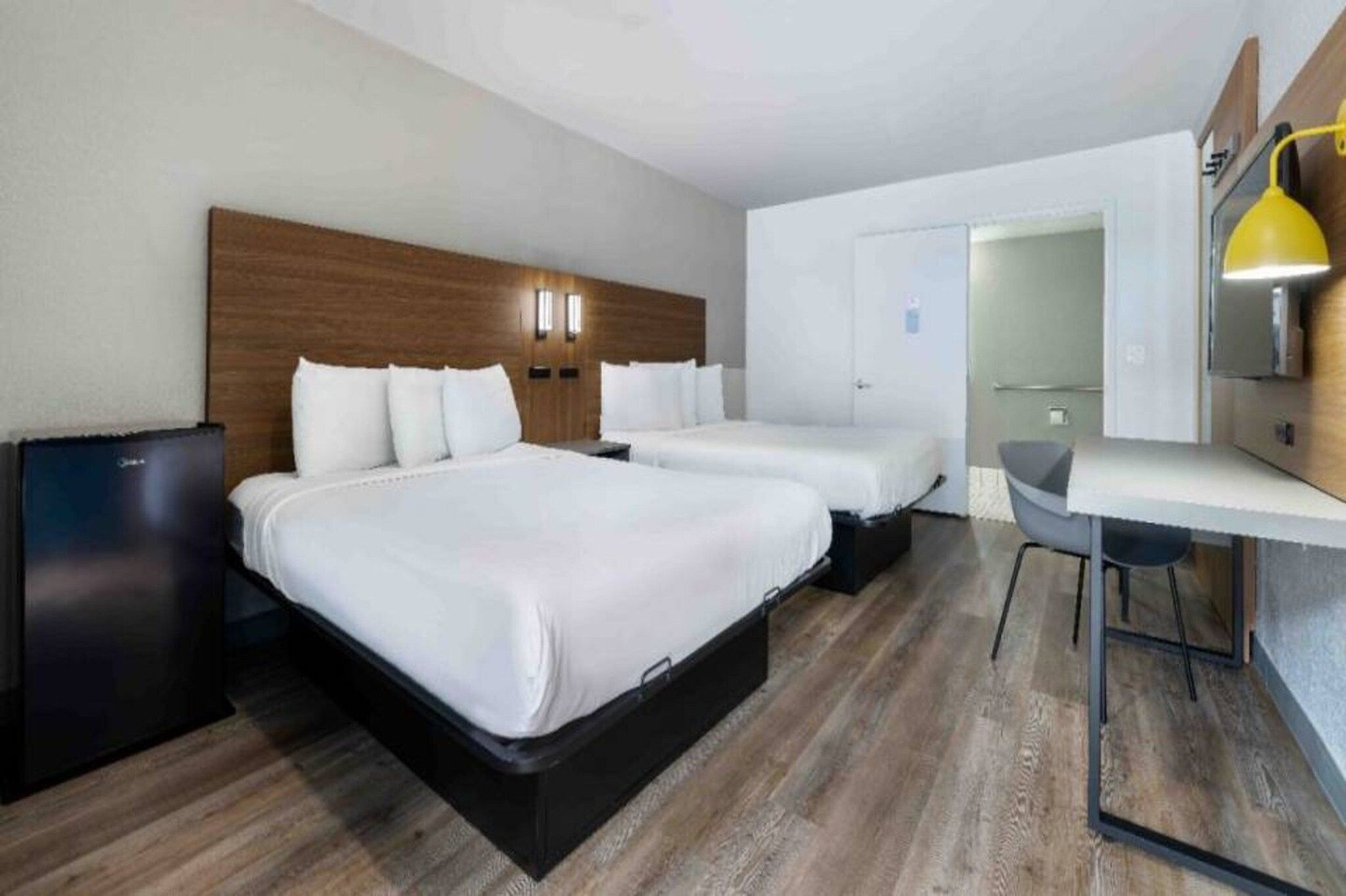 A hotel room with two beds, a desk, and a small kitchenette.