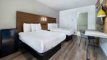 A hotel room with two beds, a desk, and a small kitchenette.