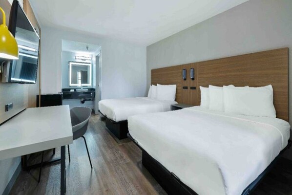 A hotel room with two beds, a desk, a chair, and a television.