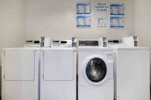 Een rij witte voorladers in een wasserette, met instructieposters aan de muur.