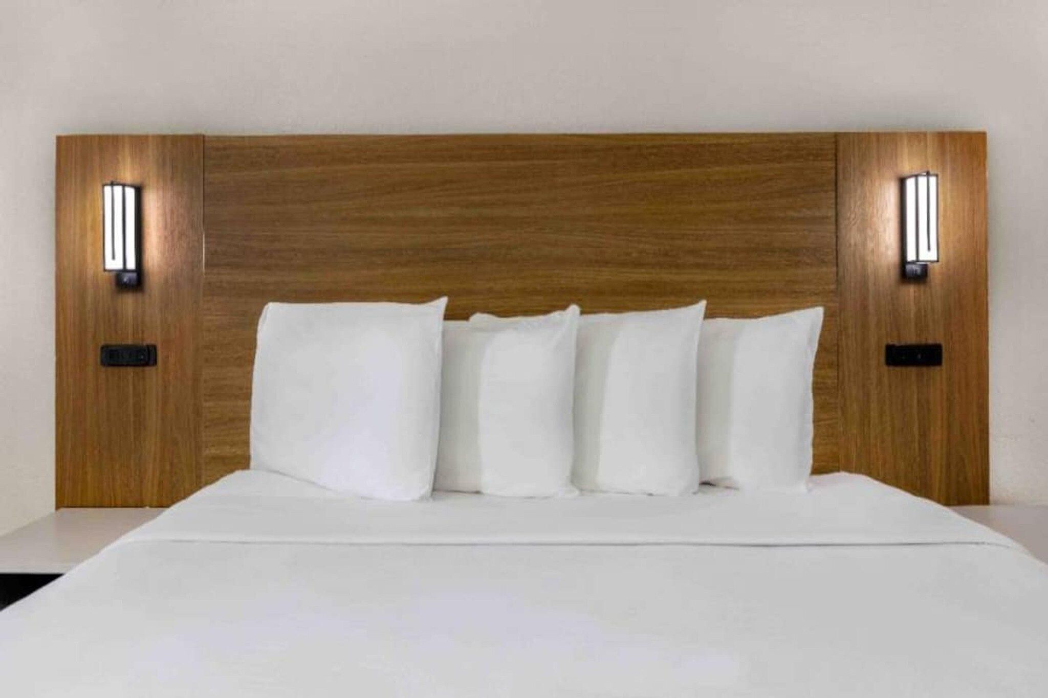 Un lit avec une tête de lit en bois et deux appliques murales, une de chaque côté.