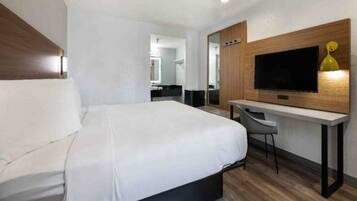 Habitación de hotel con cama, escritorio, silla, televisor y espejo.