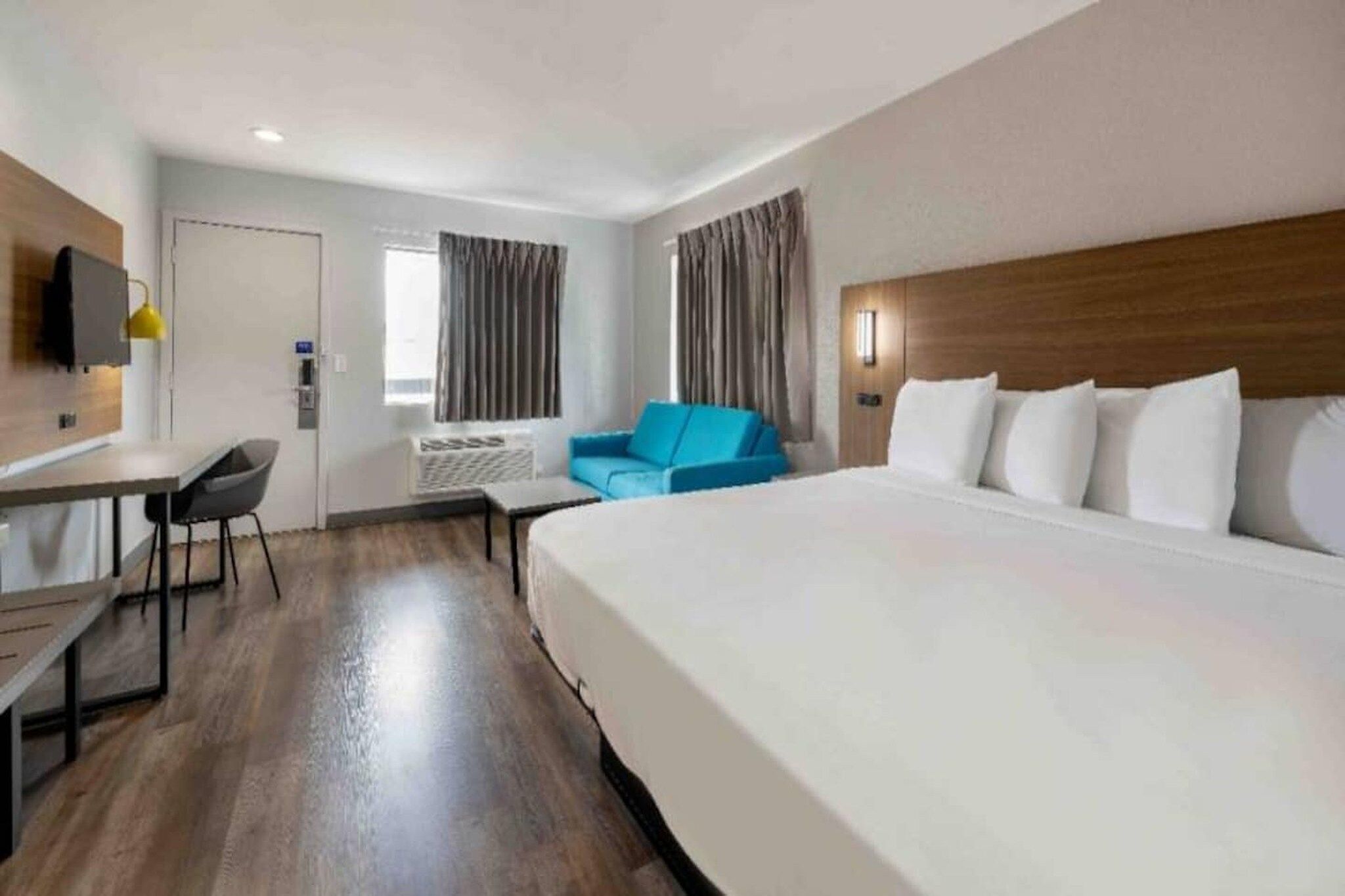 Habitación de hotel con una cama grande, un escritorio, una silla, un sofá azul y una televisión en la pared.