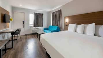 Habitación de hotel con una cama grande, un escritorio, una silla, un sofá azul y una televisión en la pared.