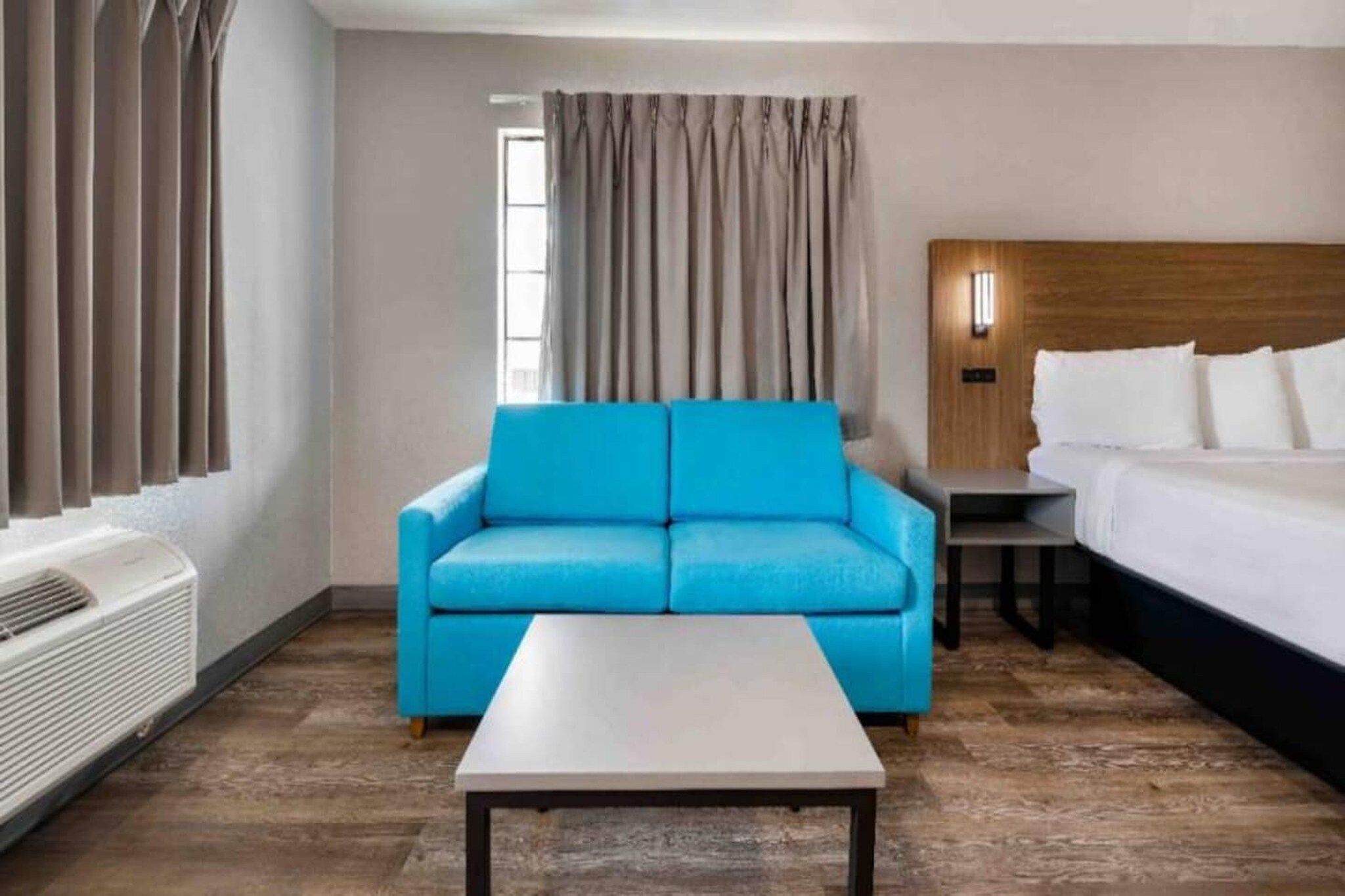 A hotel room with a blue sofa, a bed, a small table, and a window with curtains.