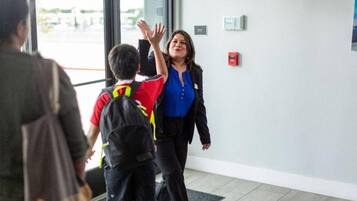 A woman in a blue blouse and black jacket walking inside a building with a child in a red and black jacket.