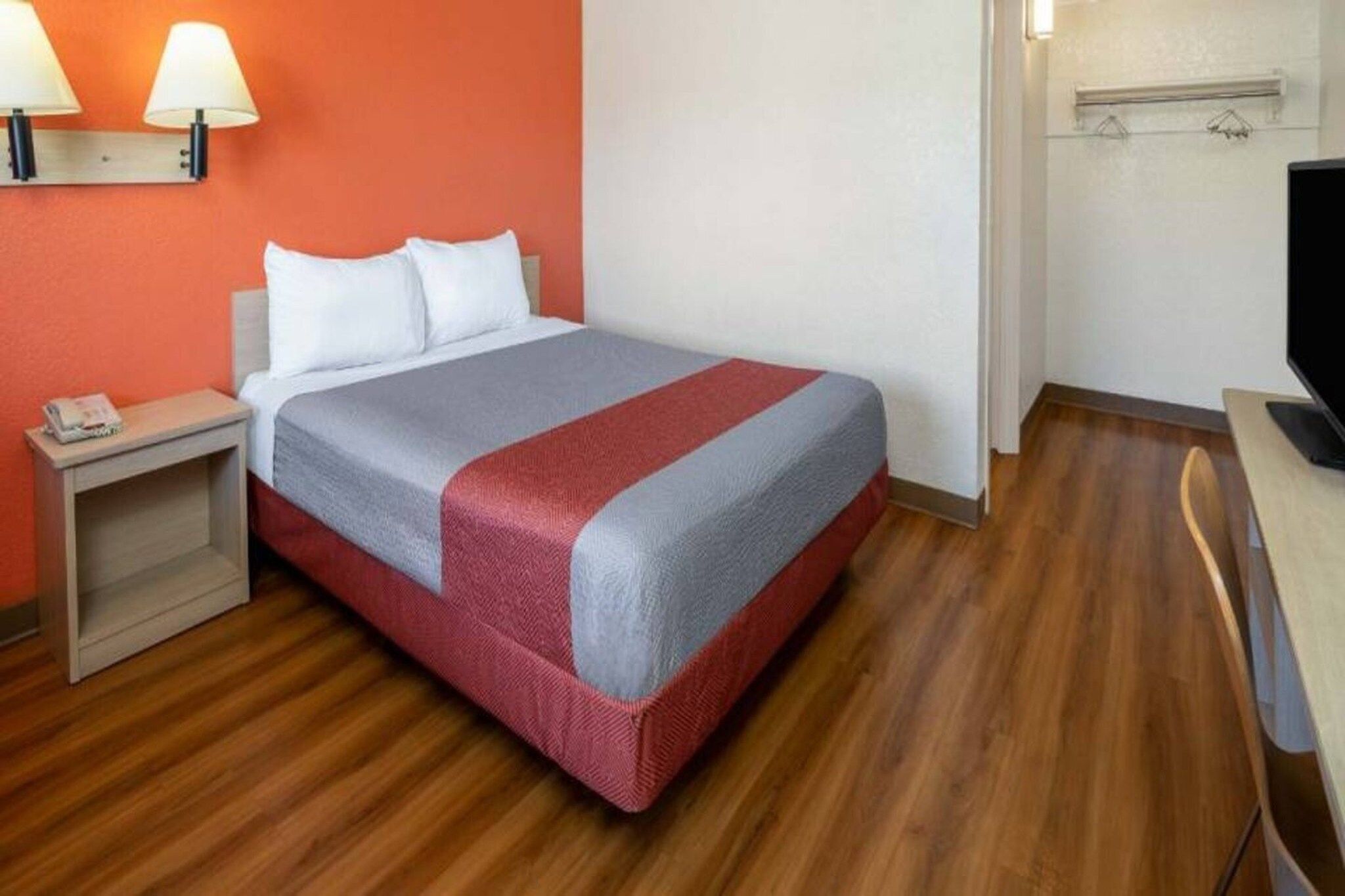 Ein Hotelzimmer mit einem Bett, einem Nachttisch, einem Fernseher und einer Wandleuchte.