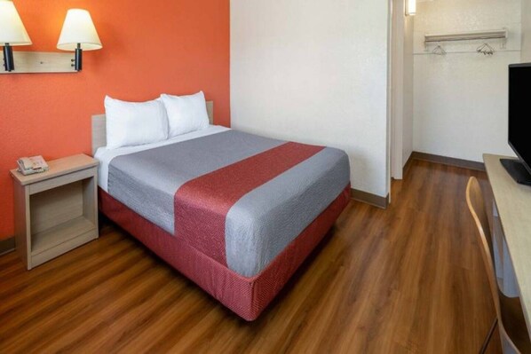 Ein Hotelzimmer mit einem Bett, einem Nachttisch, einem Fernseher und einer Wandleuchte.