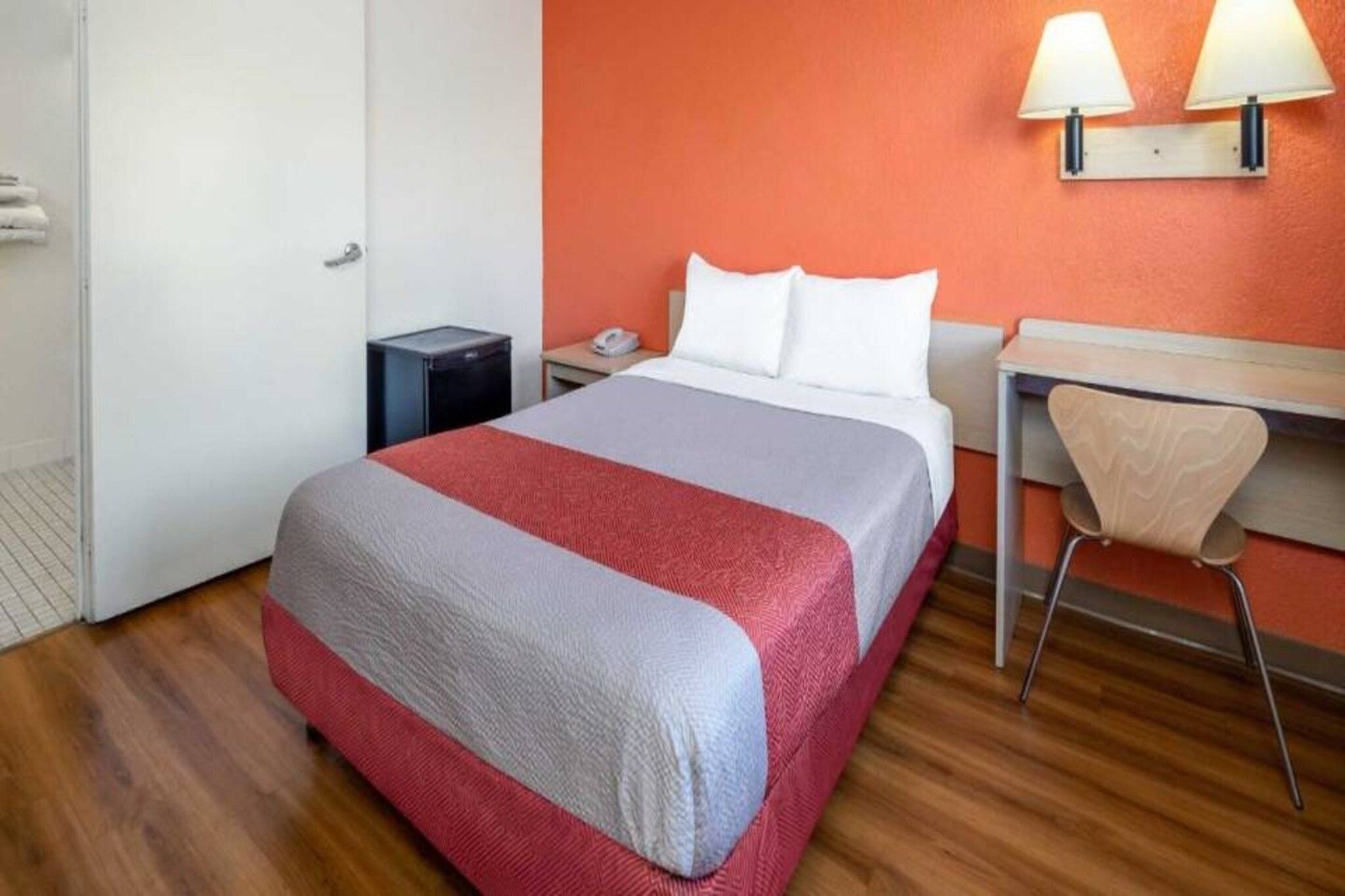 Een hotelkamer met een bed, een bureau, een stoel, een nachtkastje en een lamp.