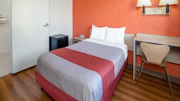 Een hotelkamer met een bed, een bureau, een stoel, een nachtkastje en een lamp.