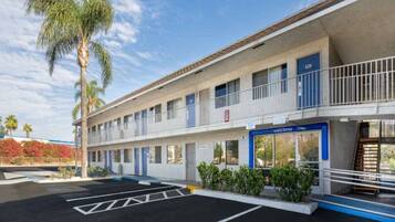 A motel with a two-story structure, a parking lot, and a palm tree.