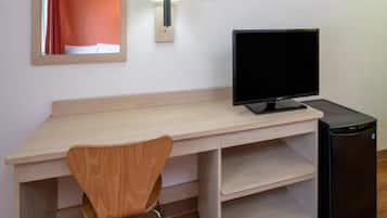 A room with a wooden desk, a black monitor, a chair, and a black refrigerator.