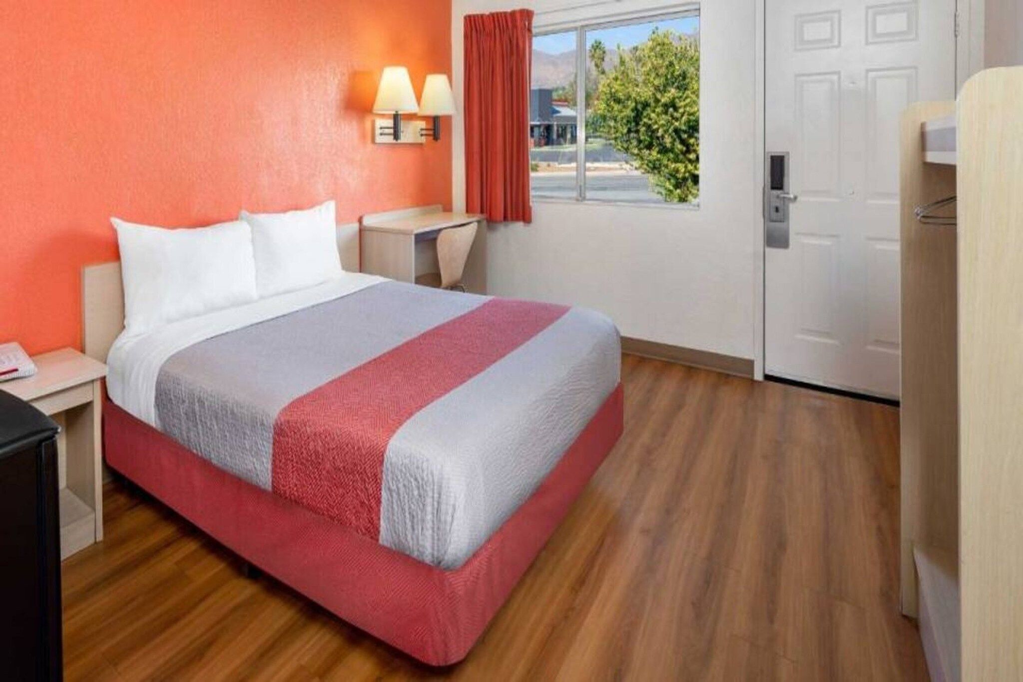 A hotel room with a bed, bedside tables, a lamp, a window with curtains, and a door.