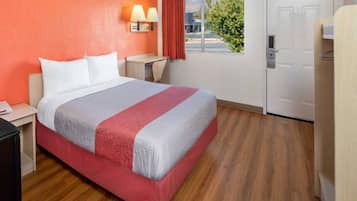 A hotel room with a bed, bedside tables, a lamp, a window with curtains, and a door.