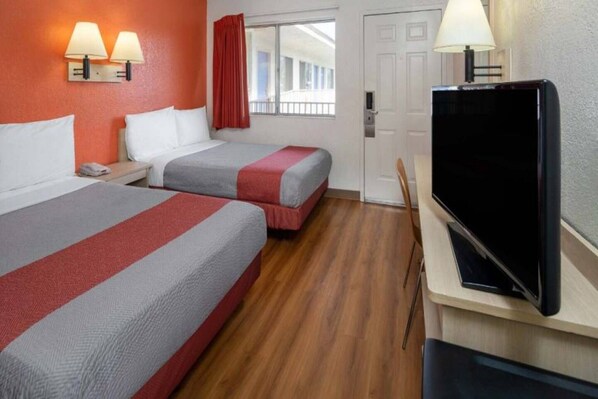 Ein Hotelzimmer mit zwei Betten, einem Fernseher und einem Fenster mit Vorhängen.