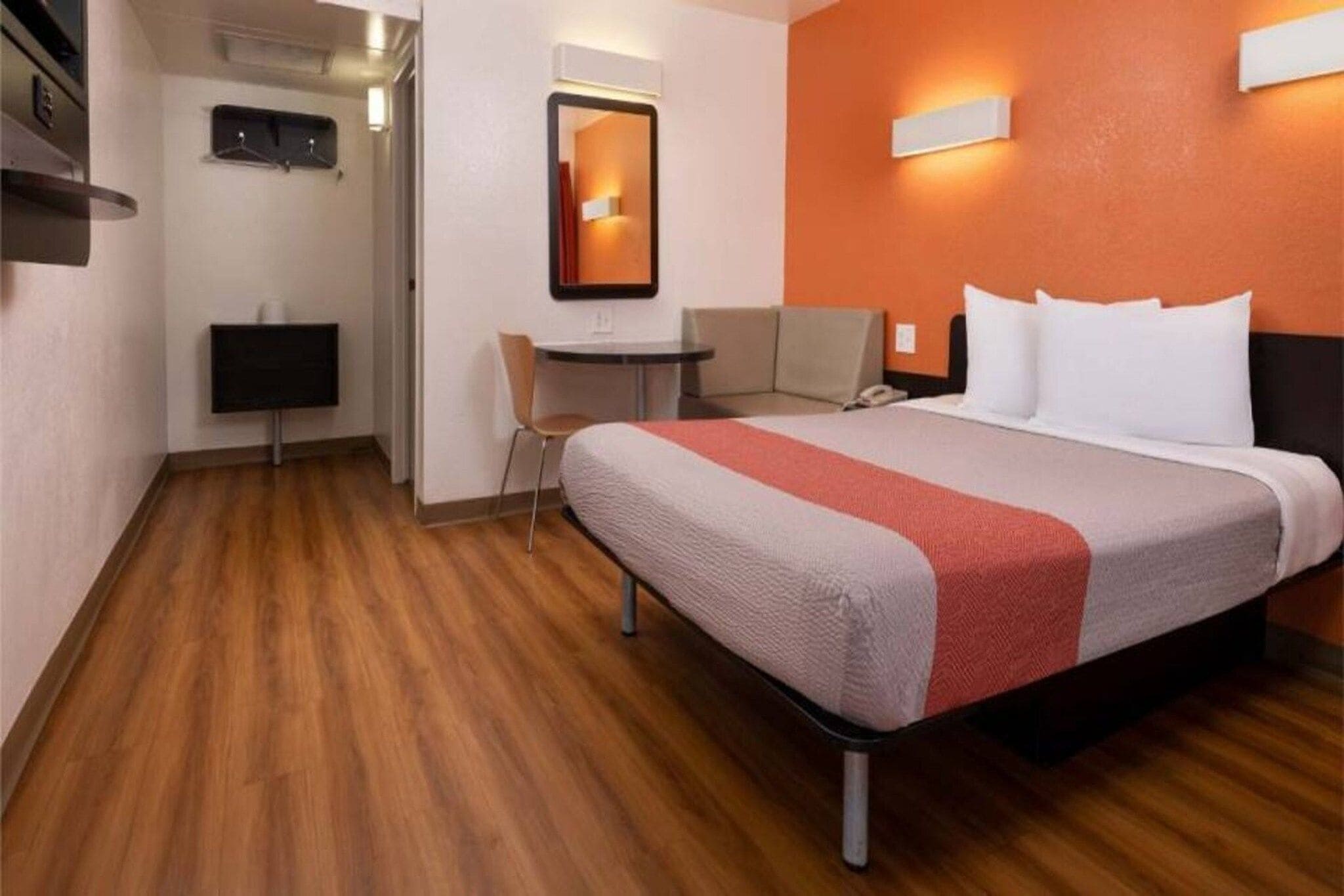 A hotel room with a bed, a desk, a chair, a TV, and a mirror.