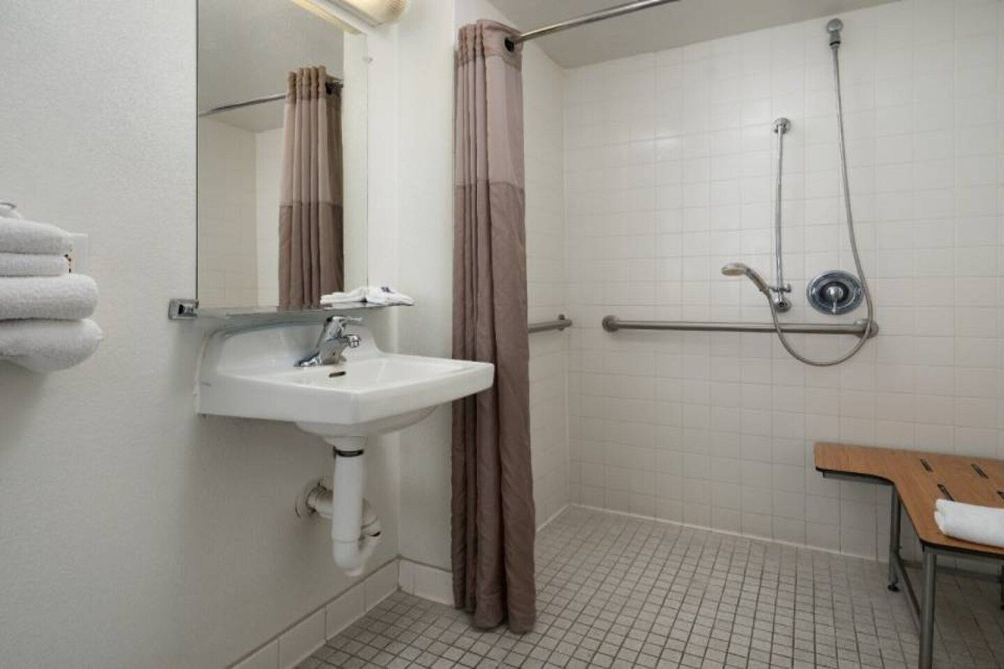 Une salle de bain équipée d’un lavabo, d’un miroir, d’une douche et d’un banc.
