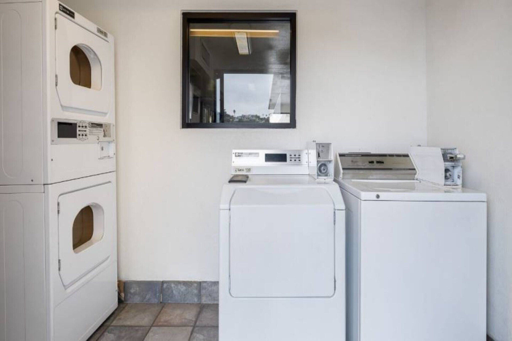 A laundry room with stacked washers and dryers, a window, and a tiled floor.