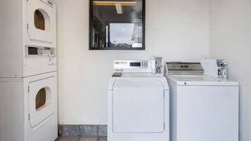 A laundry room with stacked washers and dryers, a window, and a tiled floor.