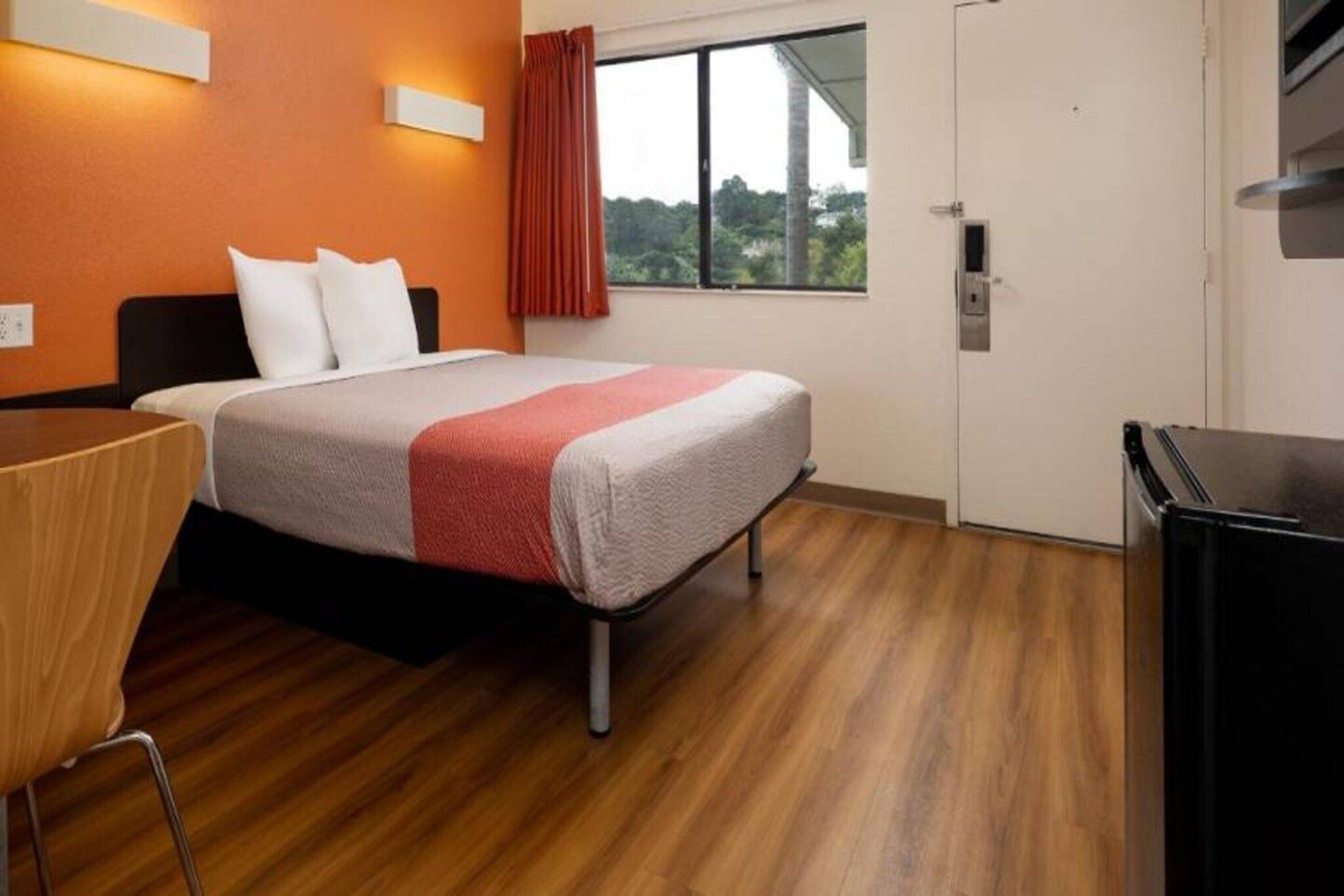 A hotel room with a bed, a desk, a chair, a wardrobe, and a window with a view of greenery.