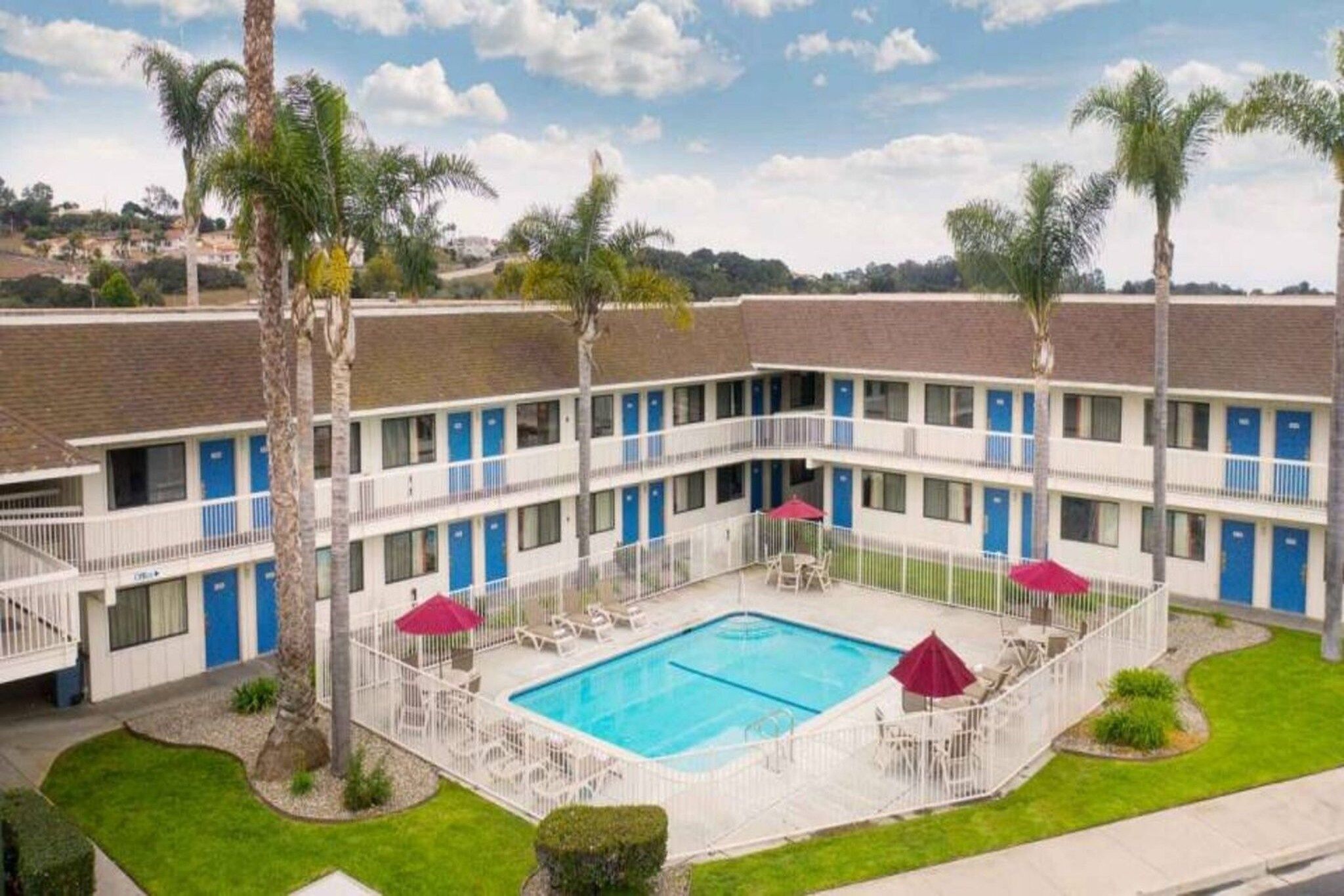 A motel with a swimming pool, multiple balconies, and palm trees.