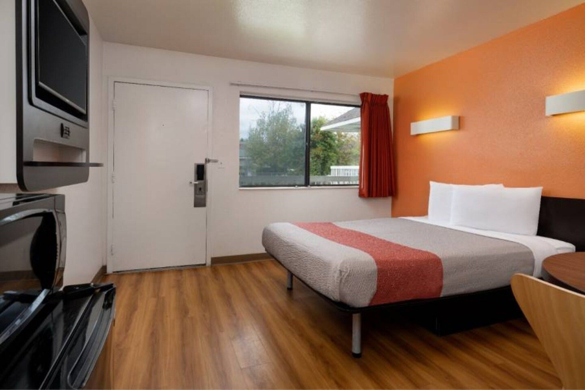 A hotel room with a bed, a desk, a television, and a window with curtains.