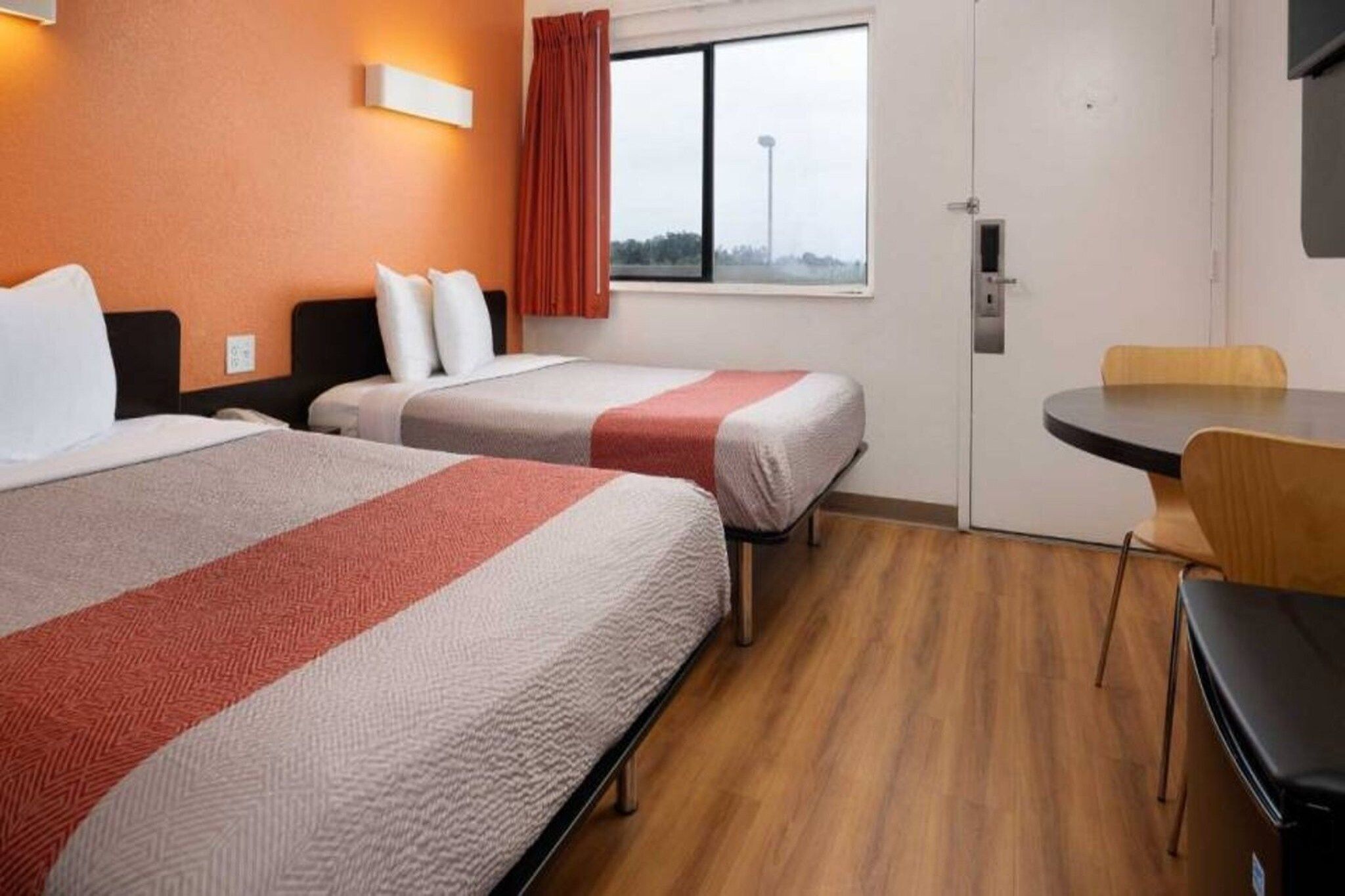 A hotel room with two beds, a window with a view, a desk, and a chair.