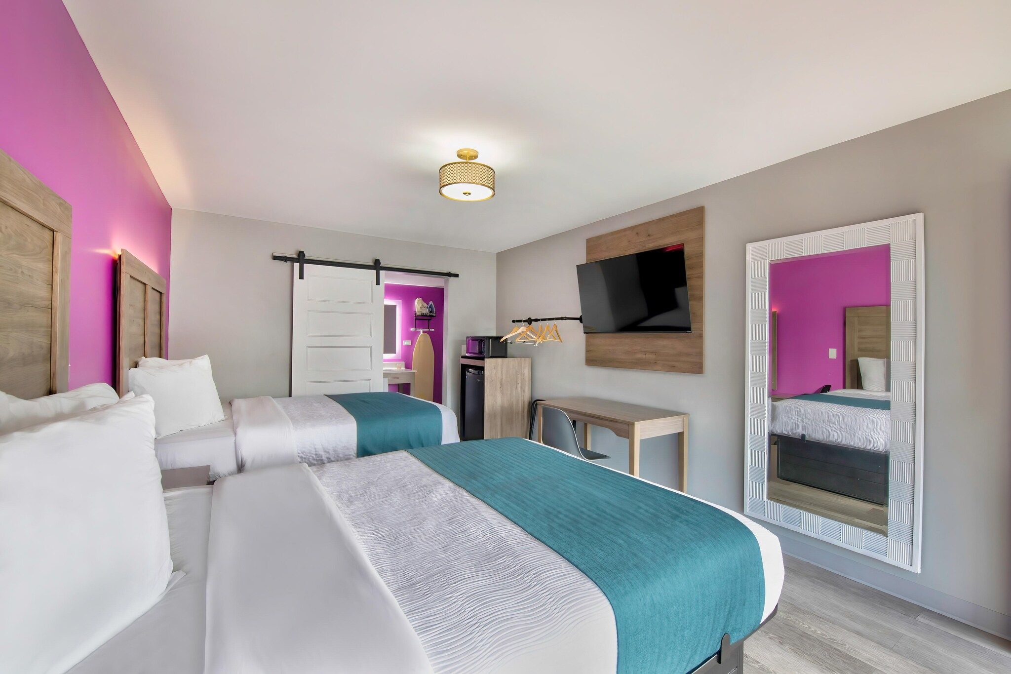 Une chambre d’hôtel avec deux lits, un téléviseur fixé au mur et une porte coulissante donnant accès à la salle de bain.