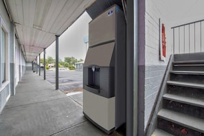 A covered walkway leading to a building with a large, modern-looking structure, possibly a vending machine or equipment, and a set of stairs leading up to a door. - 2 Full Beds | Non-Smoking (Tuscaloosa)