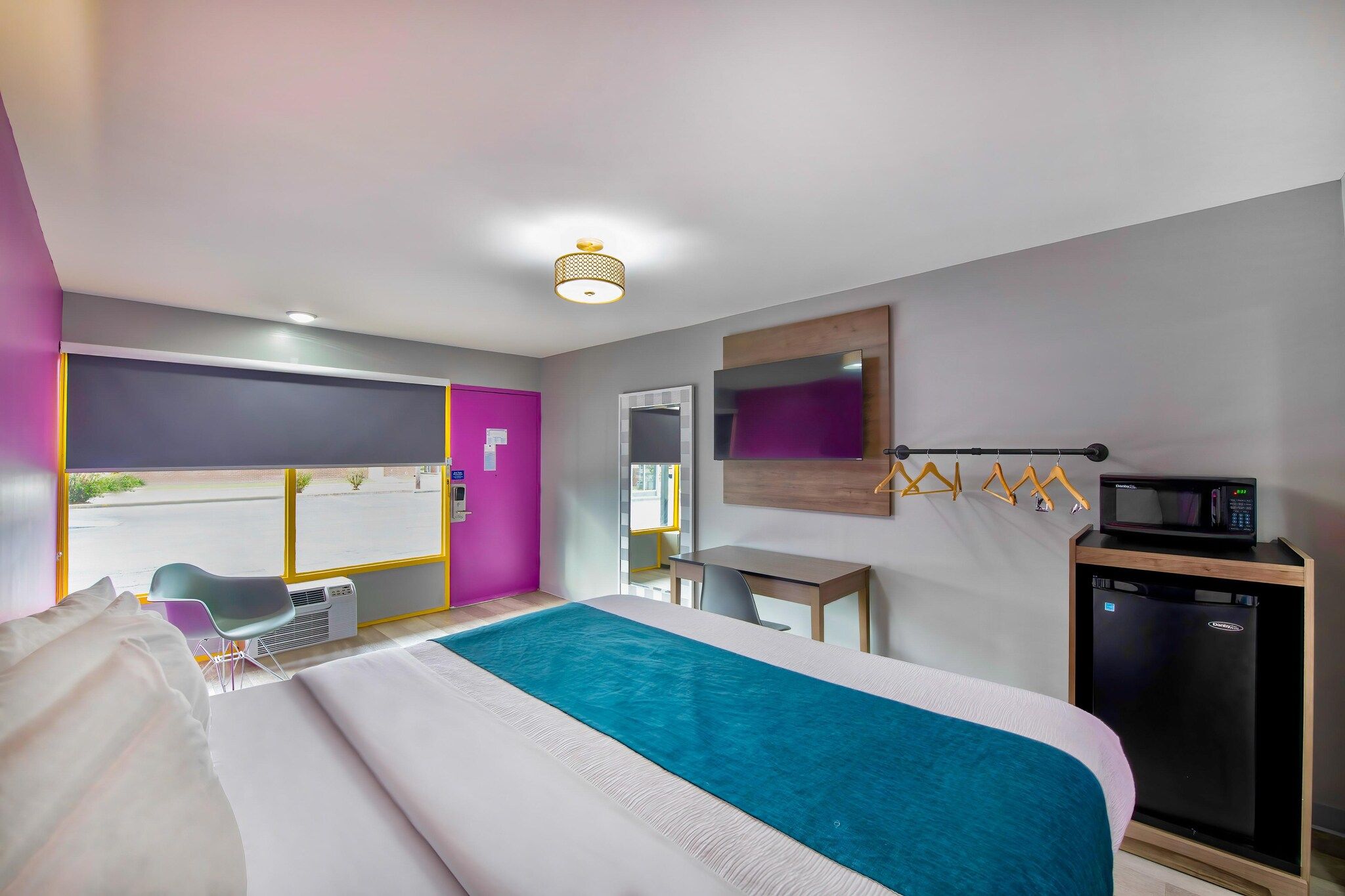 A hotel room with a bed, a desk, a chair, a microwave, and a mini-fridge.