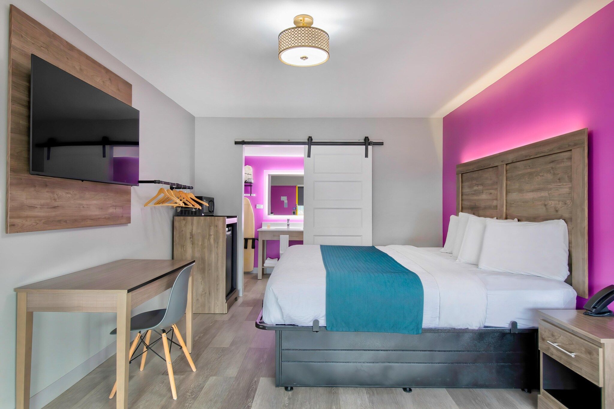 A modern hotel room with a bed, desk, chair, and a bathroom visible through an open door.