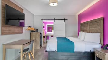 A modern hotel room with a bed, desk, chair, and a bathroom visible through an open door.