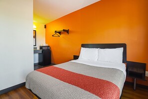 Habitació d'hotel amb un llit, una tauleta de nit, una làmpada penjada a la paret i una taula petita amb una tassa.