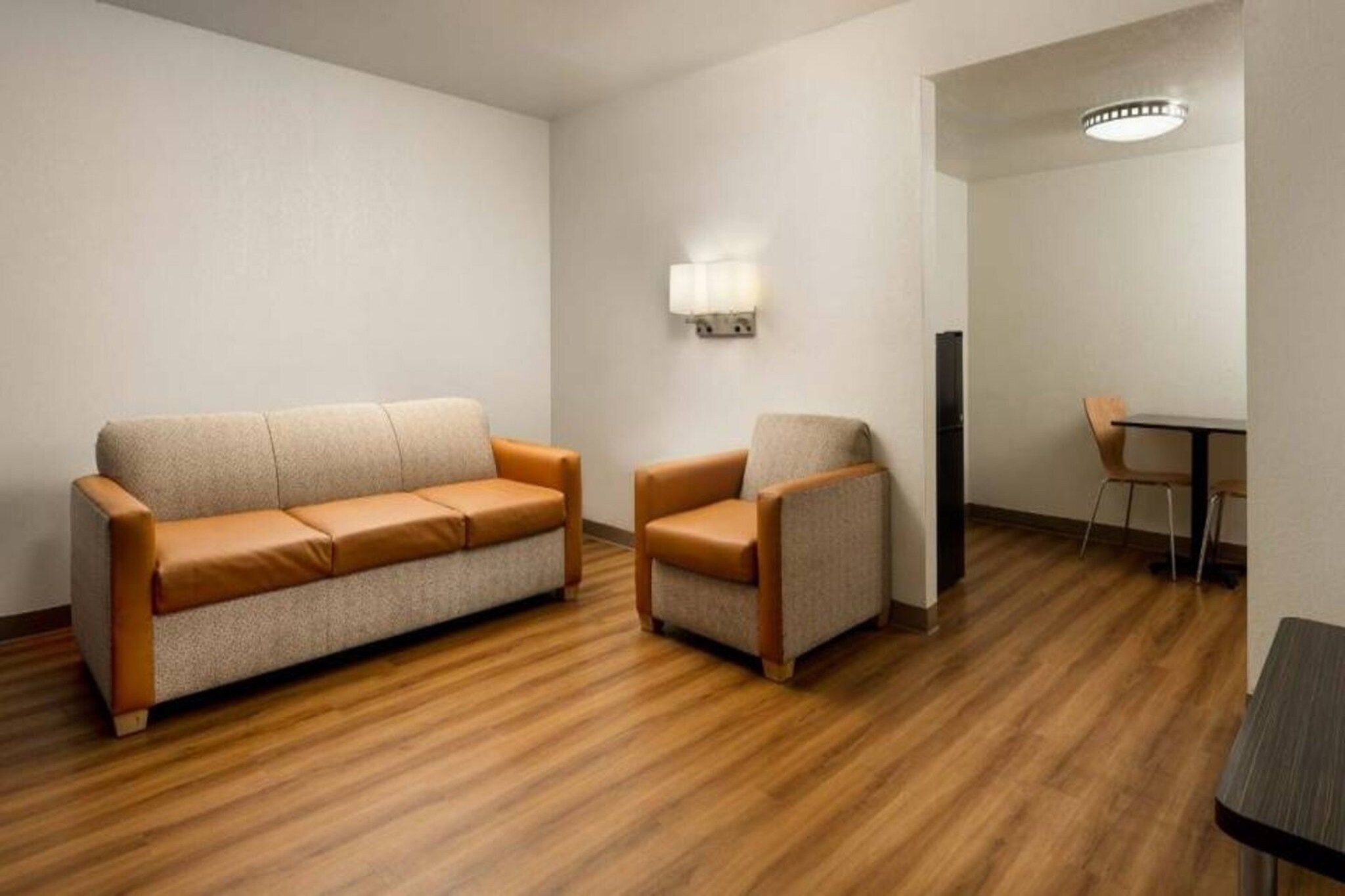 Ett rum med en soffa och en fåtölj, ett bord och en väggmonterad lampa.