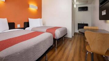 A hotel room with two beds, a dining table, and a TV mounted on the wall.