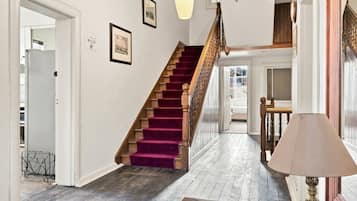 Un escalier avec une rampe en bois et une moquette violette, menant à une pièce où se trouvent un lit et une lampe.