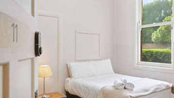 Een slaapkamer met een bed, een bedlampje, een raam met uitzicht op groen en een deur met slot.
