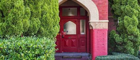 A red brick building with a red door, white picket fence, and well-maintained green hedges.